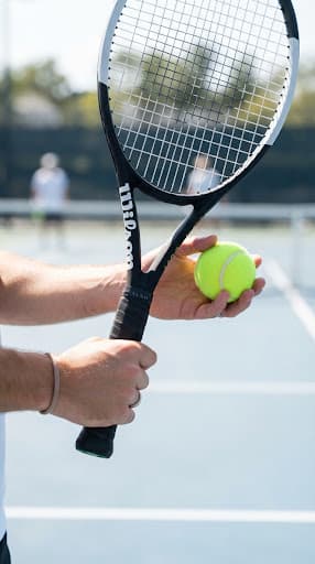 Close-up of a hand holding a tennis racket and ball